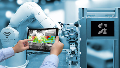 Hands holding a tablet in front of an industrial robot.