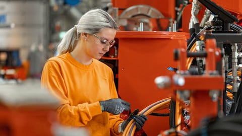 A woman in work clothes putting together machine cables in an industrial environment