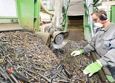 A man wearing personal protective equipment standing next to a big pile with used cemented carbide tools and inserts that are going to be recycled