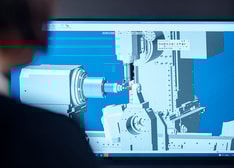 A woman looking at a computer screen with an image of a machining operation which is generated using CAM software