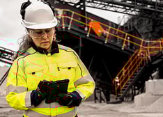 A woman in work clothes and helmet standing in front of a screening station at a quarry