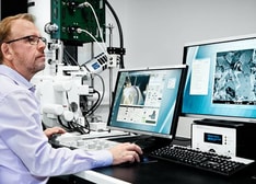 A man at a desk with a microscope and two monitors