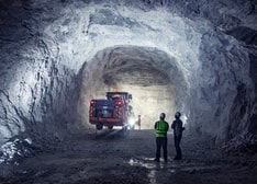 Two men standing in an underground mine looking at an underground drill rig
