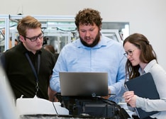 Three persons standing looking at the same laptop