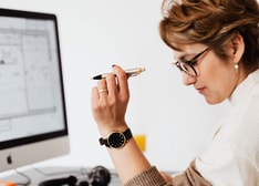 A woman sitting at a desk with a computer screen displaying a schematic drawing