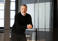 A man in his forties leaning against a railing in an office environment