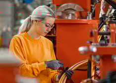 A woman in work clothes putting together machine cables in an industrial environment