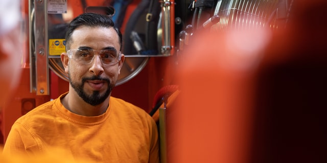 A man wearing safety glasses standing in front of a large machine in a industrial environment