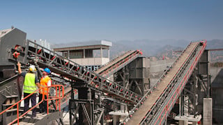 Two men standing at the top of a conveyor system at a rock processing plant