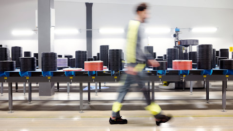 A man in work clothes passing a long bench with trays with inserts on it in an industrial setting