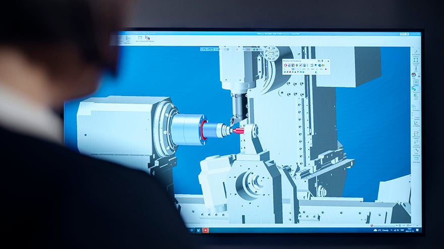 A woman looking at a computer screen with an image of a machining operation which is generated using CAM software