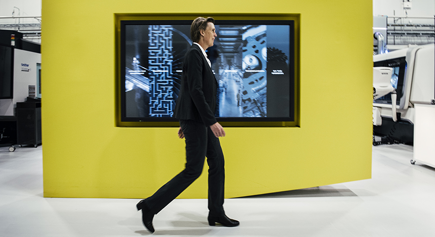 A woman in a suit walking past a yellow wall with a large monitor on it