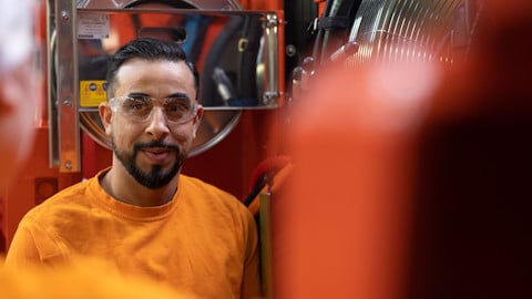 A man wearing safety glasses standing in front of a large machine in a industrial environment