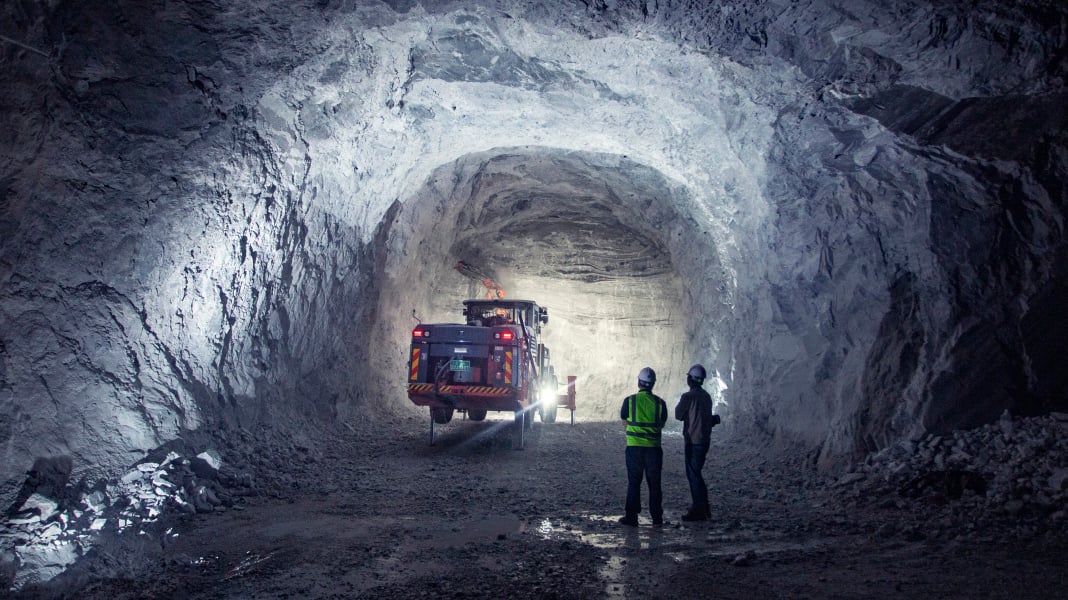 Two men standing in an underground mine looking at an underground drill rig