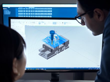 A woman and a man looking at a computer screen with an image of a toolpath for a milling operation which is generated using CAM software