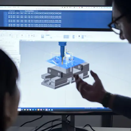 The heads of a woman and a man next to a computer screen displaying software simulating machining operation