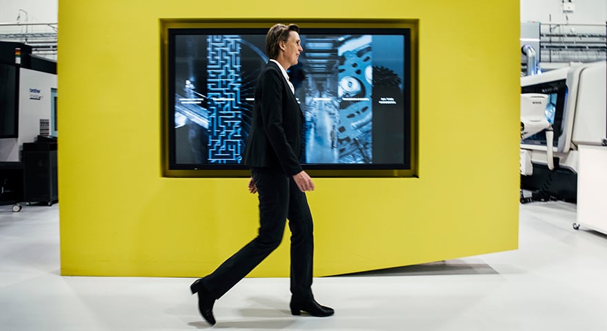 A woman in a suit walking past a yellow wall with a large monitor on it